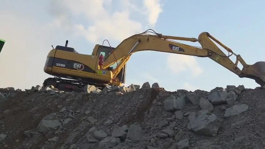 Excavator working blasted rock at the quarry face